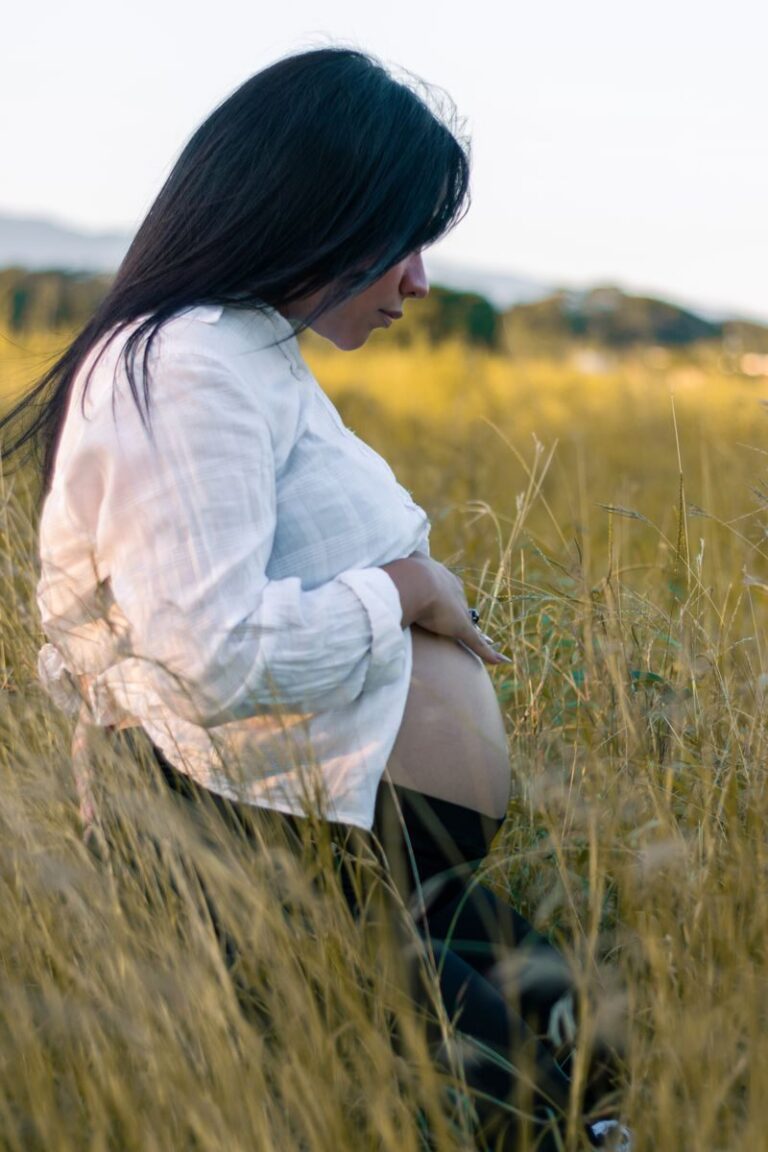 A serene maternity photoshoot in a sunny meadow in San Felipe, capturing a pregnant woman in a white shirt.